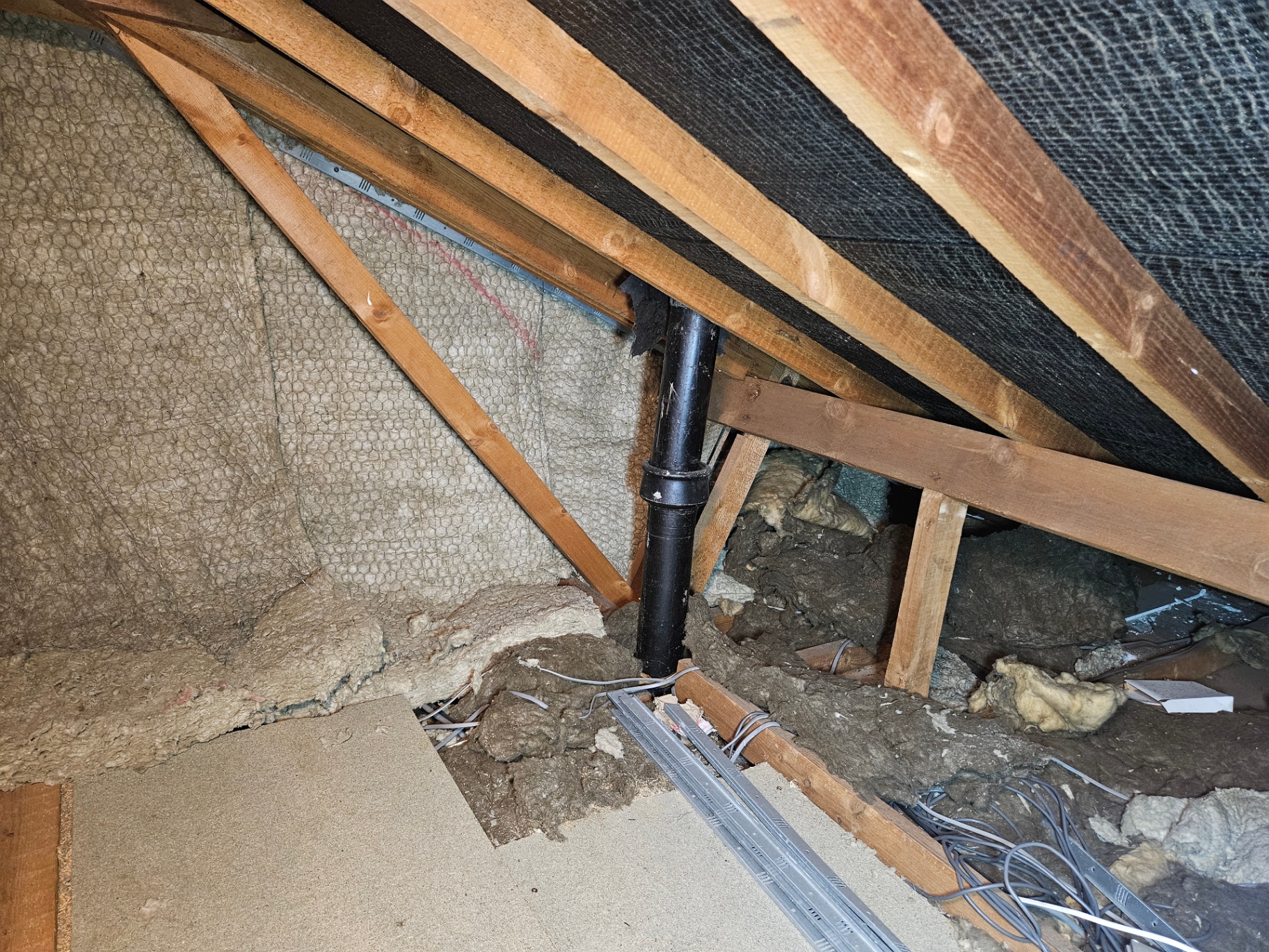 Loft Pipe Lagging & Loose Insulation Brown fibrous lagging wrapped around an old soil pipe in a loft, surrounded by loose mineral wool insulation between rafters.