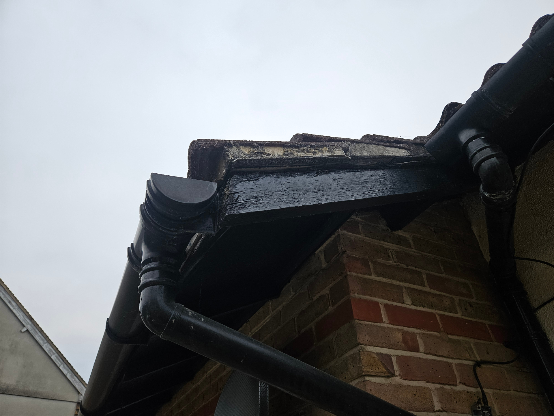 Damaged Soffit Board at Eaves Damaged soffit or eaves board at a roof edge beside black rainwater goods, with exposed weathered board material visible along the return.