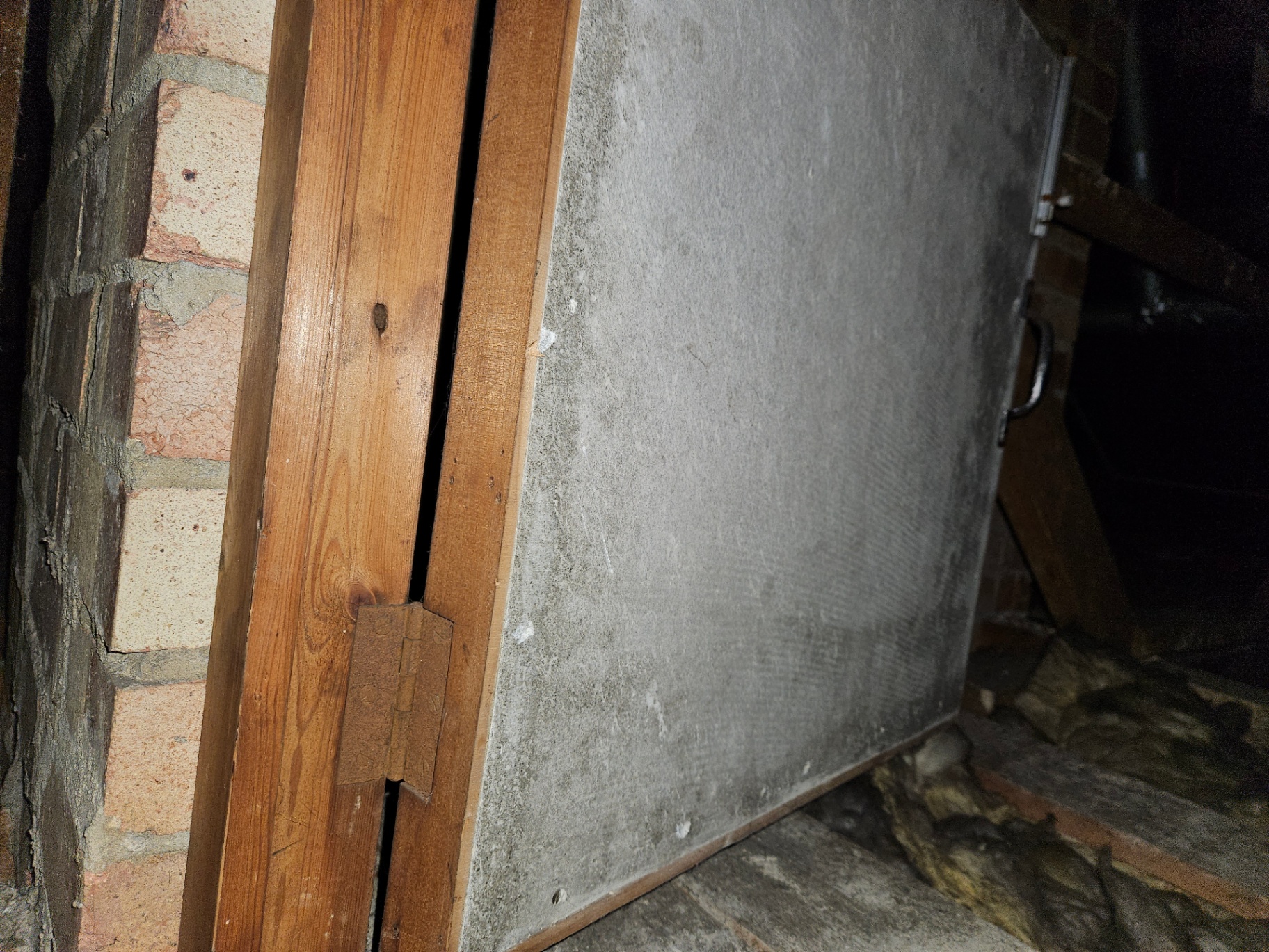 AIB Cupboard Door – Fireplace Recess Grey asbestos insulating board fixed to a timber frame forming a small cupboard door beside a brick chimney.